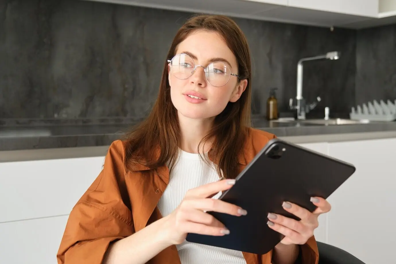 Портрет молодой красивой женщины в очках, работающей из дома и обучающейся онлайн на своей кухне.